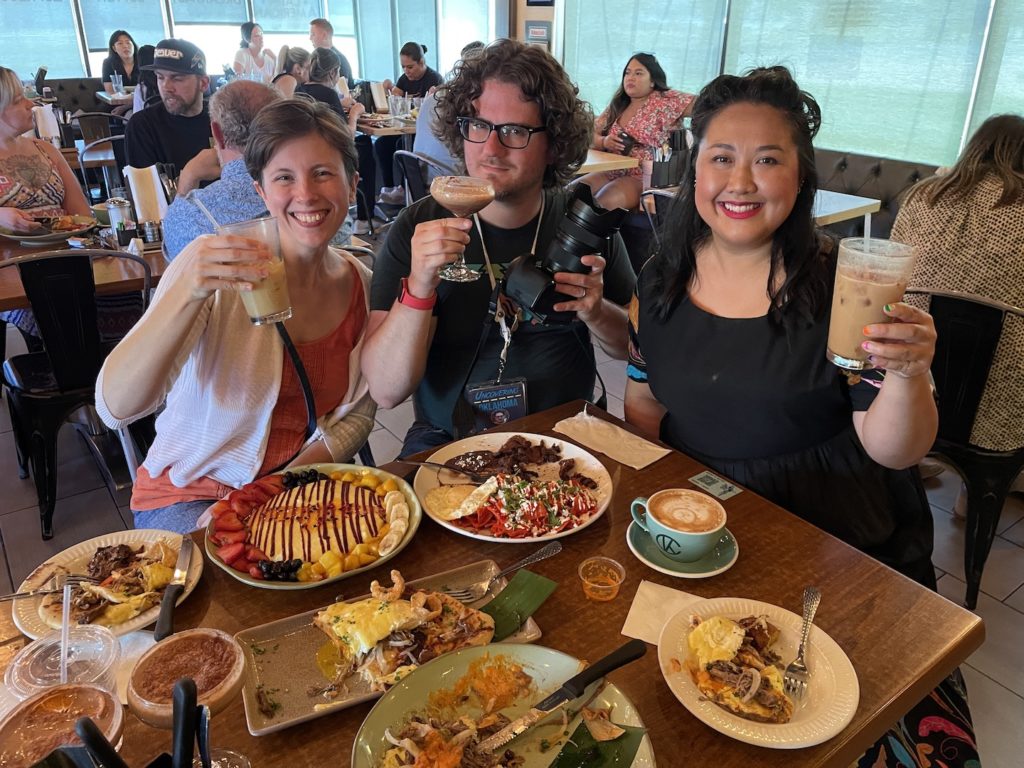 Photograph of Lessa, Dennis, and Phi holding up drinks inside the restaurant Cafe Kacao.