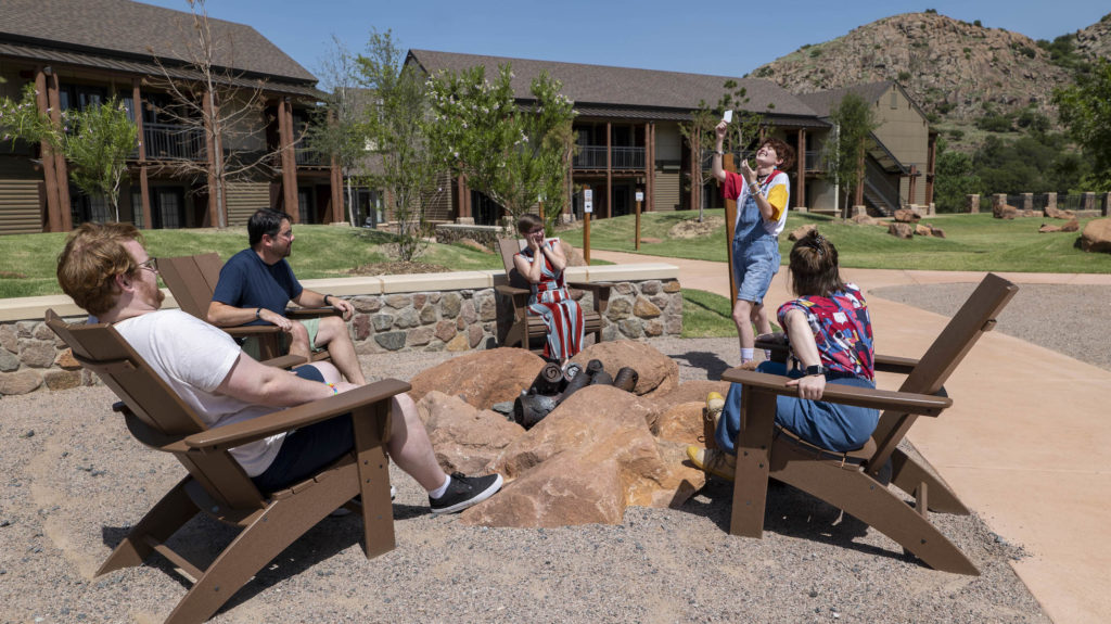 A photographic reference of five young adults gathered around a fire pit as one of them holds up a black card