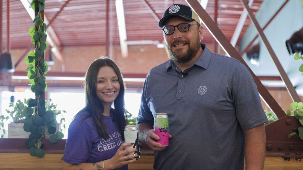 Photo of Bri holding a can of beer while standing with the owner of Skydance Brewing.