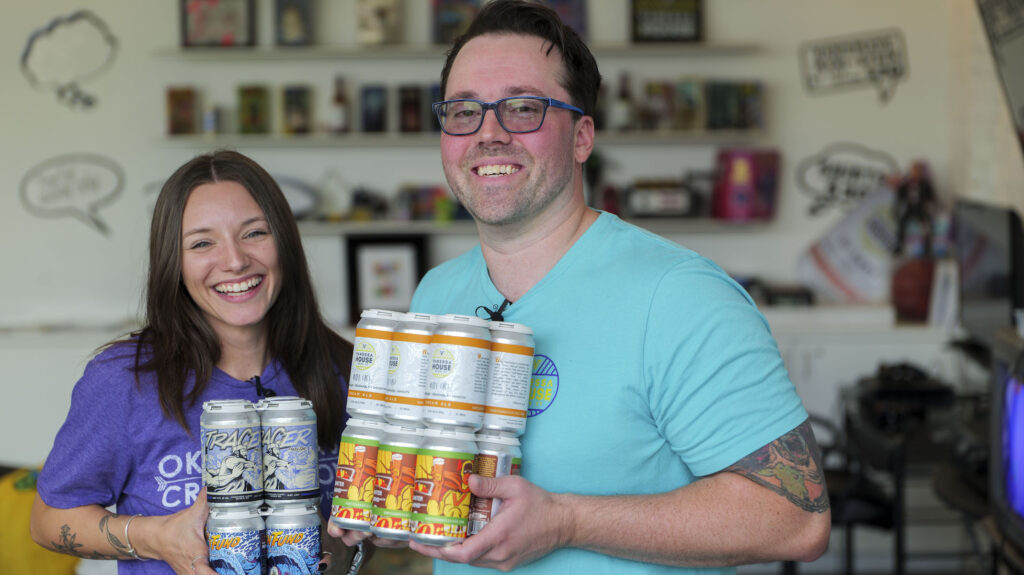 Photo of Bri holding up cans of beer from Vanessa House Beer Company with co-owner, Andrew Carrales.