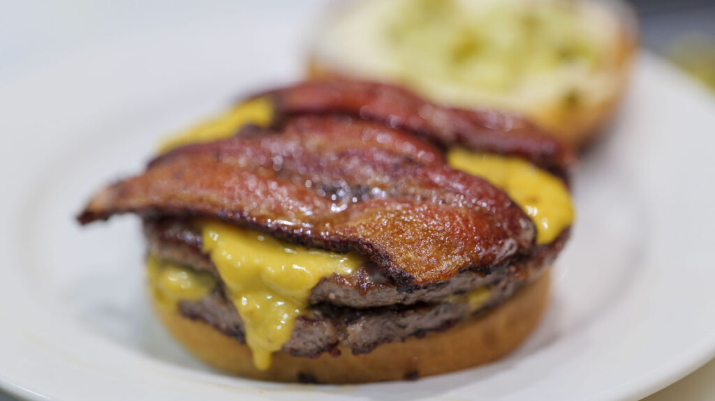 Photo of the Thick Cut Bacon from New State Burgers & Spirits on a double cheeseburger. 